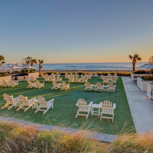 Lawn chairs on a grassy patch pointed towards an ocean sunset