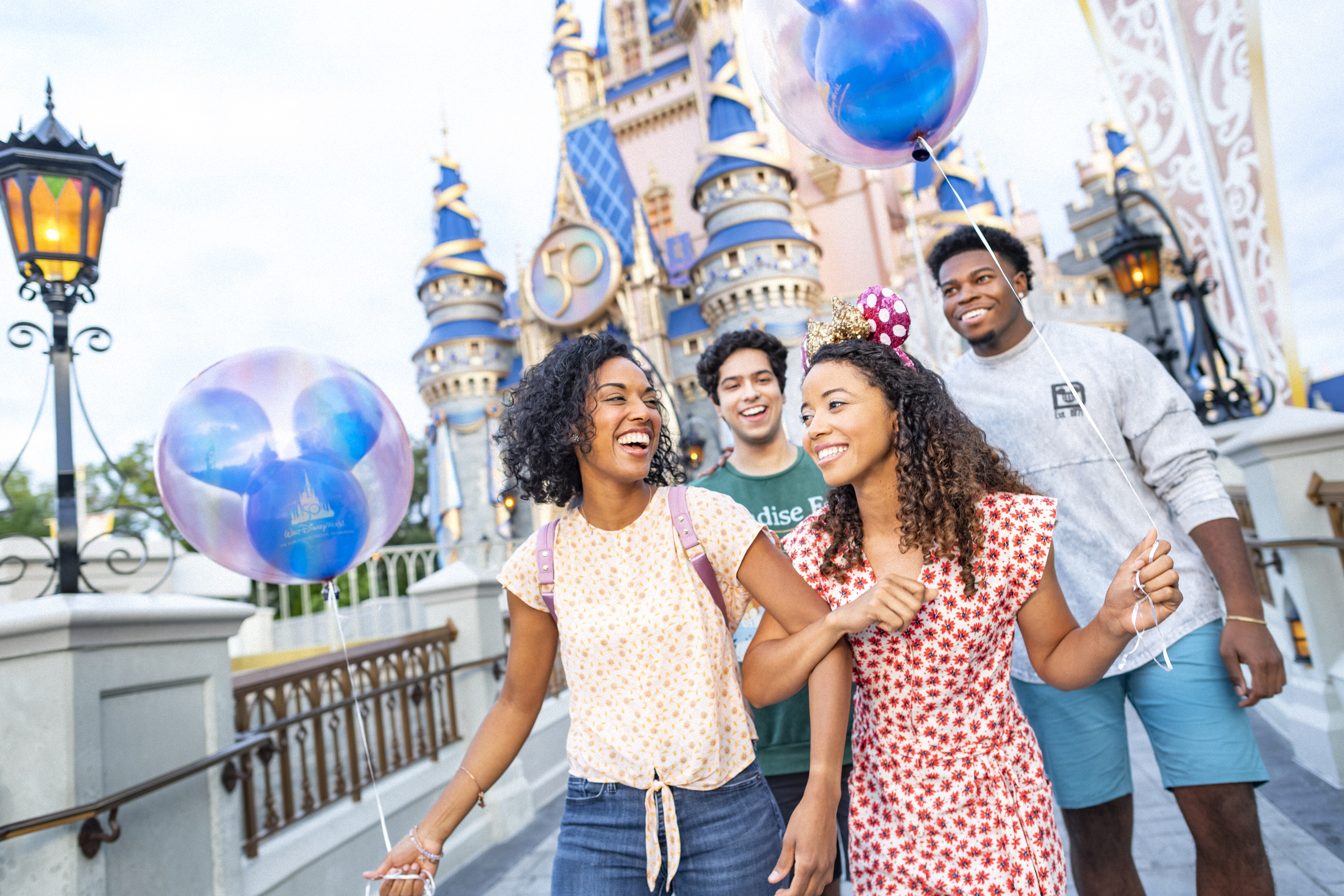 Group of friends walking by Disney Castle with Mickey Mouse Ear Balloons